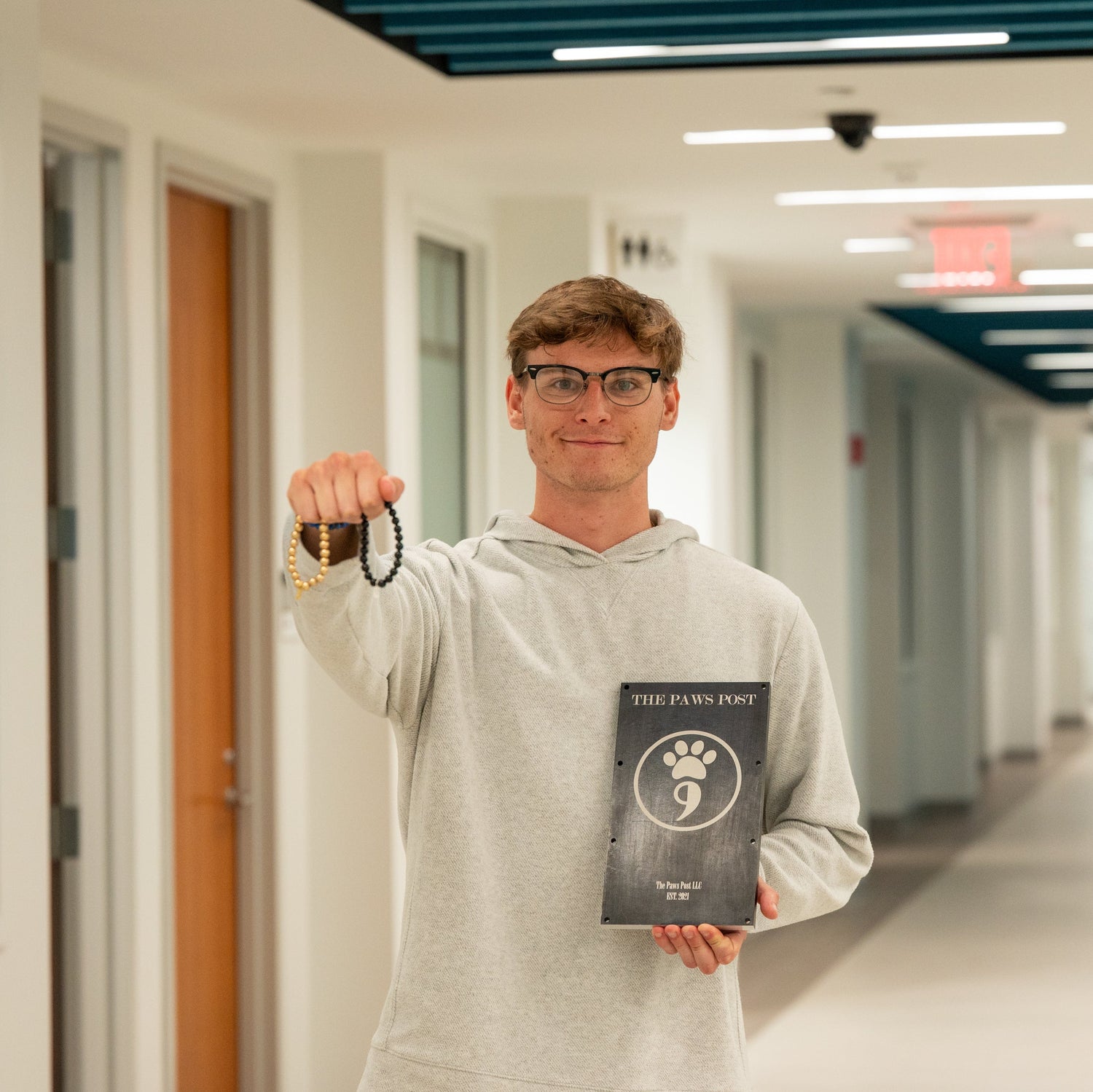 Person holding a plaque titled 'The Paw's Post' in the Sprague Center hallway at Bryant University
